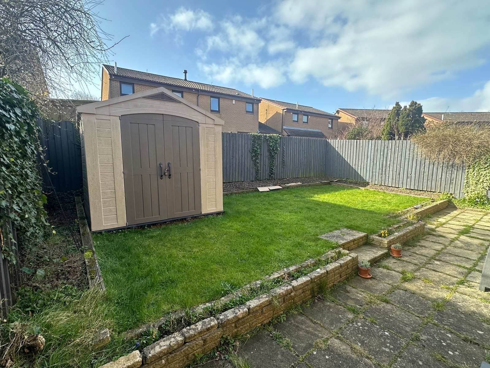 A modest back garden with a raised lawn, stone retaining wall and beige shed
